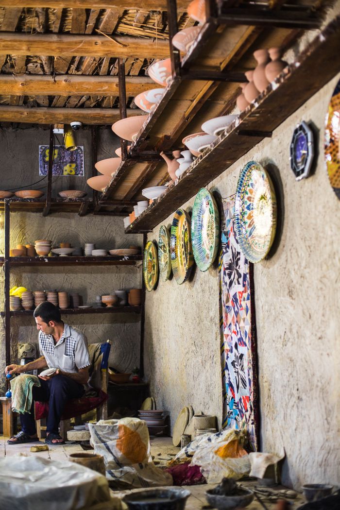 our-stories A craftsman creates pottery in a workshop adorned with colorful plates in Gijduvon, Uzbekistan.